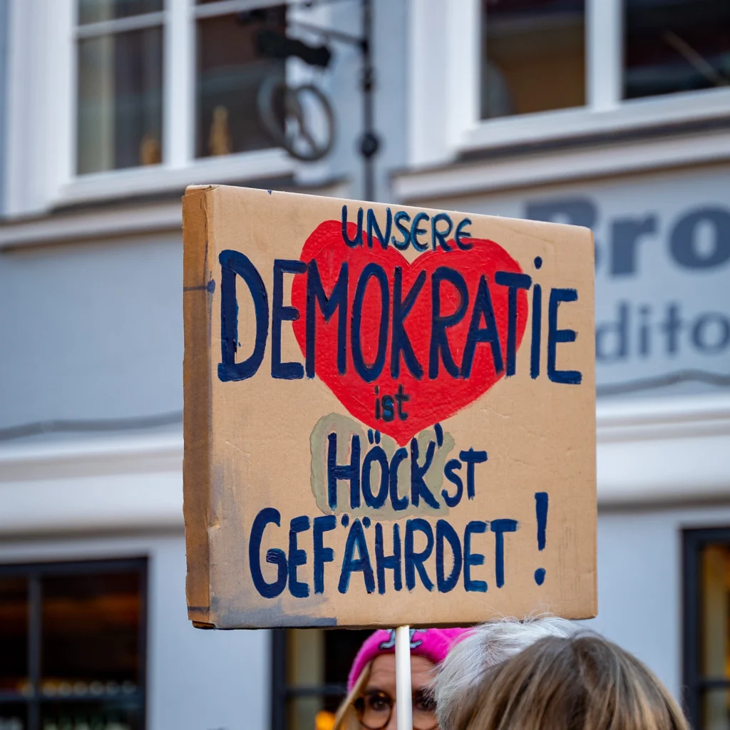 Auf dem Bild ist ein Schild einer Demonstration zu sehen. Darauf geschrieben steht: Unsere Demokratie ist Hockst gefährdet.